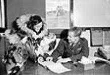 [Joanne Adjun (left), Cecile Kamingoak (centre), William Kamingoak (infant) getting their monthly family allowance at the old government office.] 1949-1950