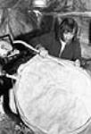 [James Koighok fabriquant un tambour à la maison. La peau de caribou servait autrefois à fabriquer des tambours; elle a été remplacée par de la toile.] 1949-1950