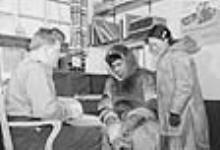 Un couple inuit accompagné d'un agent de la GRC.[(De gauche à droite) : agent non identifié de la Gendarmerie royale du Canada(GRC), et Oluqsie et Mucklpah en visite au bureau de la GRC.] 1949 - 1950