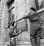 Lieutenant-Colonel R.S. Malone (left) helping to erect the sign at the editorial office of the Maple Leaf newspaper, Caen, France, 11 July 1944 July 11, 1944.