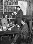 Mrs. Freda Cooper of the Canadian Red Cross playing cribbage with Private W.J. Downey while Private J.C. Veilleux browses in the library of No.18 Canadian General Hospital, Royal Canadian Army Medical Corps (R.C.A.M.C.), Colchester, England, 15 December 1944 Deember 15, 1944.