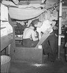 AB C.G. Walker using saw to cut bread aboard H.M.C.S. GEORGIAN 1944