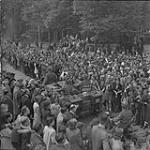 Canadian troop carrier passes through crowd of Dutch civilians along route taken when liberating the Netherlands 7 May 1945