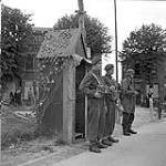 Privates W.R. Hill and M.A. Gammon of 1st Canadian Corps on guard duty with a German soldier, also on guard duty, at the German garrison, Ijmuiden, Netherlands, 11 May 1945 May 11, 1945.
