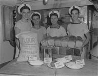 The bakery staff of H.M.C.S. UGANDA stands behind a stack of their "International Loaves" 6 Aug. 1945