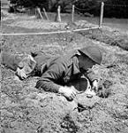 Le Sapeur C.W. Stevens, 18e compagnie de campagne du Corps royal du génie canadien, utilise un miroir pour repérer les allumeurs sous une mine allemande Teller 22 June 1944