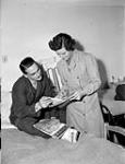 Senior Welfare Officer Dorothy King of the Canadian Red Cross delivering copies of Canada's Weekly to Signalman N.L. Grant at No.2 Canadian General Hospital, Royal Canadian Army Medical Corps (R.C.A.M.C.), Ghent, Belgium, 11 December 1944 Deember 11, 1944.