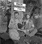 Sergeant Johnny Wayne and Staff-Sergeant Frank Shuster of the Canadian Army Show's "Invasion Revue" wearing captured German uniforms beneath a sign which reads, "Nach Dunquerke 7 Km.", Bergues, France, 16 September 1944 September 16, 1944.