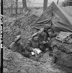 Queen's Own Cameron Highlanders of Winnipeg Ptes. W. Repeta and H. Sundin, L/Cpl. R. Poirier and Pte. O.G. Bugg opening a parcel in a pup tent covered German dugout. Hochwald Forest, Germany 5 Mar. 1945 5 MAR. 1945
