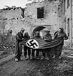 Canadian soldiers displaying a large German flag removed from a fortified house 9 mars 1945