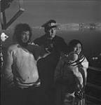 Constable Ed Jones of the Royal Canadian Mounted Police (R.C.M.P.) watching the shore from the ship D'IBERVILLE with special constable Minkyoo and his wife - Twin Glacier trip Aug. 1953
