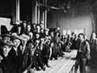 Groupe de personnes autour d'une table de nettoyage du grain, dans une ferme expérimentale non identifiée du ministère de l'Agriculture ca 1910 - 1930