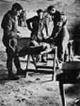 Major P.K. Tisdale, 4th Field Ambulance, R.C.A.M.C., checking the condition of a wounded man before Sergeant W.H. Brigham and Private L.P. Lemieux donate blood before his transfer to a Field Surgical Unit 15 jan. 1944