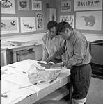 Iyola Kingwatsiak and Eegyvudluk Pootoogook, Inuit artists, working on a stone block in the art centre, Cape Dorset, N.W.T., [(Kinngait), Nunavut], August 1961 August 1961.