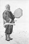 [Inuk man, James Koighok, in a caribou parka playing a qilaut (drum) with a qatuk] Inuit man in a caribou parka playing a qilaut (drum) with a qatuk 1949.