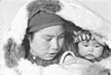 Close-up photograph of a woman carrying her infant in an amauti at Inukjuak, Nunavik (Quebec) [Martha (née Nulukie) Nowra and her daughter Louisa (née Nowra) Elijasialuk] Martha (née Nulukie) Nowra was married to Josie (Juusi) Nowra. 1947-1948.