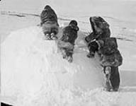 Nanook and men of his hunting party putting finishing touches on the snow 'Igloo' built in an hour ca. 1910-1921