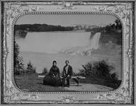 Un homme et une femme assis sur un banc, devant les chutes vers 1865.