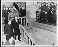 Rt. Hon. Clement Attlee and Viscount Alexander of Tunis descending stairs during an official function. Mr. W. Howard Measures is immediately behind the Royal Canadian Mounted Police (R.C.M.P.) constable ca.1949