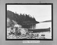 [Innu (Montagnais) on the shore of Grand Lake with Chief Swashine sitting, on left]. Original title: Montagnais Indians on the Shore of Grand Lake. Chief Swashine sitting. ca. 1930