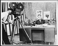 Robert N. Thompson during television recording. CKCK-TV cameraman filming at left 1965