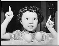 Chinese New Year, old Chinese legend, eggs stand on end at New Years. Lorraine Louie, 6, daughter of Mr. and Mrs. Kwok Sun Louie, shows evidence ca. 1962.