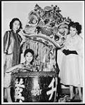 On friendly terms with a symbolic Lion's Head are Lorraine Jong, Mei-ling Ko, and Olive Mark, as they modelled Chinese dresses at a pageant in support of the annual United Appeal for charitable organizations Oct. 1959
