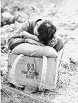 Un jeune Coréen, fatigué de transporter une lourde caisse de rations « C-6 » qu'il apporte aux troupes canadiennes à la ligne de front. Sa fatigue pourrait aussi être attribuable au fait qu'il a débuté sa journée aux petites heures du matin 16 Apr. 1951