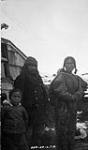 [Inuit man, woman in skin clothing with child on back and young boy at left in front of partially seen building] Original title: Natives 17 septembre 1924
