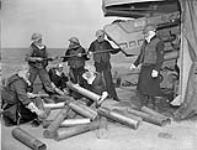 A 4.7-inch (12 cm) gun crew of the destroyer HMCS Algonquin piling shell cases and sponging out the gun after bombarding German shore defences in the Normandy beachhead June 1944.