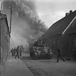 4th Canadian Armoured Division's drive towards Oldenburg under counter-attack by German Paratrooper Regiment. Street scene showing Canadian troops and tanks, and smoke from burning buildings fills thesky 10 Apr. 1945