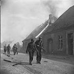 4th Canadian Armoured Division's drive towards Oldenburg under counter-attack by German Paratrooper Regiment. Street scene showing German prisoner under escort and building roof on fire 10 Apr. 1945