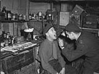 Officers of the 5th Field Regiment - Major Frank A. Robertson is being given a medical examination by Captain Doug Blue 1 - 2 Feb. 1945