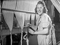 Helene Lalonde, ouvrière de fabrication de textiles à la manufacture de textiles de la Montreal Cottons, est assise devant un métier à tisser et « rentre des bouts » vers mars 1942