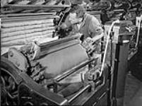 Un ouvrier, à la manufacture de textiles de la Montreal Cottons, vérifie le coton lors du processus de « cardage », qui nettoie et étire les fibres afin de les renforcer vers 1945