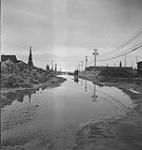 View along unpaved street flooded by melting snow May 1943