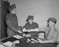CANADIANS IN GERMANY. Soldiers receive pay in German marks. L. to r.: L/Cpl. Ken Nicholls, Sgt. Harold Johnston and Capt. Frank W. Woods 09-Jul-45