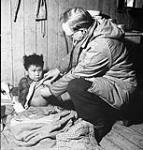 Twice yearly, native settlements are visited by a government doctor. Shown here is T.J.Orford, doctor and agent for the James Bay district, with a child showing signs of tuberculosis. The child will be hospitalized "outside" at government expense Jan. 1946