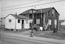 Child on road in front of tarpaper-covered house 1973