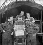 Soldiers reading the first issue of the Maple Leaf. L. to r. (front): Capt. Jack Crawford, Sgt. Clarence Rowllinson, Lt. John Farnan; (back): Ptes Gerry Vachon and Phil Jackson 28-Jul-44