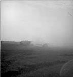 Self-propelled guns, obscured by the smoke of their own firing, in the early daylight July 1944