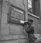 Capt. Placide Labelle adds notice on the sign for Canadian Maple Leaf Offices 11 July. 1944
