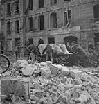 Civilians and soldiers pushing a cart of food through the rubble 10 July. 1944