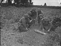 Unidentified sappers of the Royal Canadian Engineers (R.C.E.) examining an unexploded German 15.5 cm. shell, Caen, France, 10 July 1944 July 10, 1944.