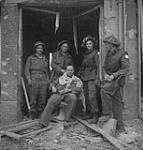 Soldiers in a barber shop in ruin. From left to right: Gnr. Vic Black, Riflemen George Cochrane, Sam Howat, Jim McCulloch, and sitting Gnr. Allan Greenwood 10-Jul-44