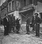 Captain DeMun (?), a French liaison officer with No.211 Detachment, talking with French civilians who have just returned to their damaged businesses and homes 10-Jul-44