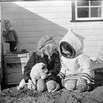 Fillette inuite et Wendy Anderson (gauche), fille du gérant du poste de traite de la Compagnie de la Baie d'Hudson, George Anderson, tenant un petit chien husky. [La fille à la droite est Rosie, fille de Jim Kilabuk et sa femme Alookie. Son nom de femme mariée était Rosie Okpik.] Août 1946