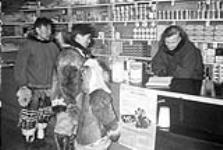 [New Hudson's Bay Co. store was built in 1949. Here William Joss is shown issuing Family Allowances in this new store to a group of Inuit] Original title: New Hudson's Bay Co. store was built in 1949. Here William Joss is shown issuing Family Allowances in this new store to a number of natives 1950