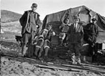 William Harold Grant (à gauche) et un groupe de personnes dans un village près du poste de la Hbc. [De gauche à droite : William H. Grant, Niiquq Inuujaq, Arnaujaq et deux inconnus. La photo a été prise à la Compagnie de la Baie d'Hudson.] 2 Septembre 1922