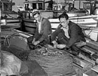 Two fishermen removing the bait from their lines. They were ready to go to sea when war was declared and the Japanese-Canadian fishing fleet was impounded 9 Dec. 1941